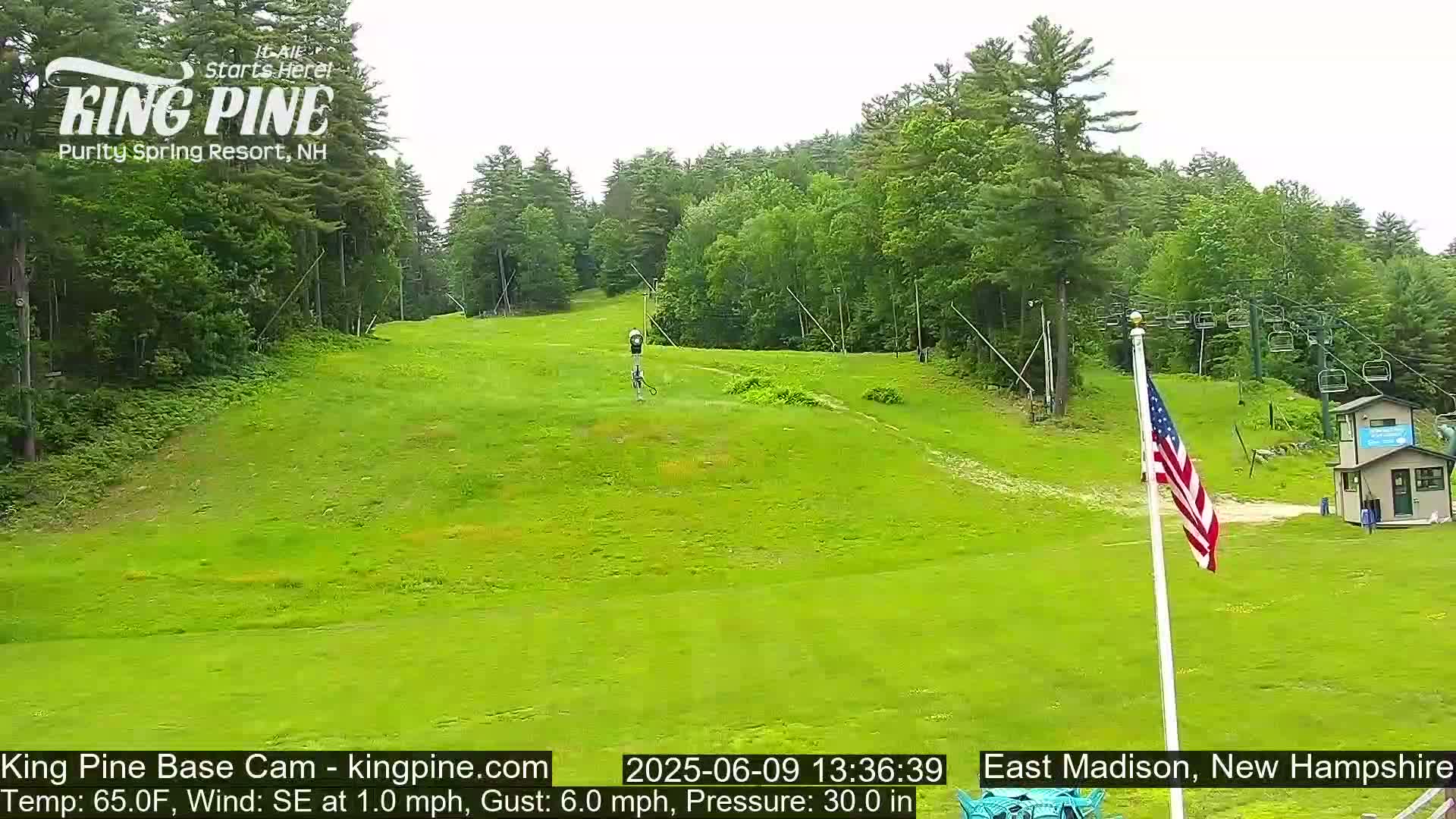 A grassy hill with a ski lift and a small building in the background under partly cloudy skies.