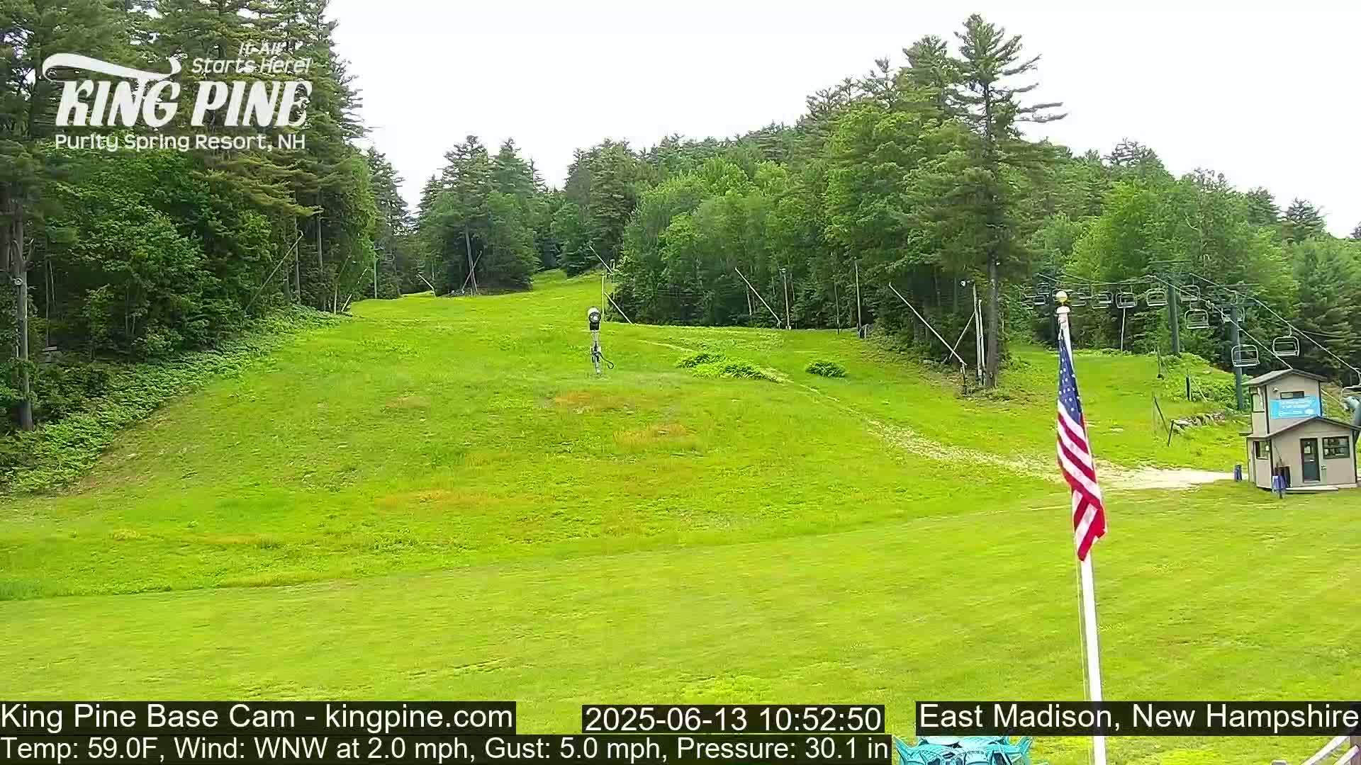 A grassy hillside with a ski lift and an American flag, under overcast skies.