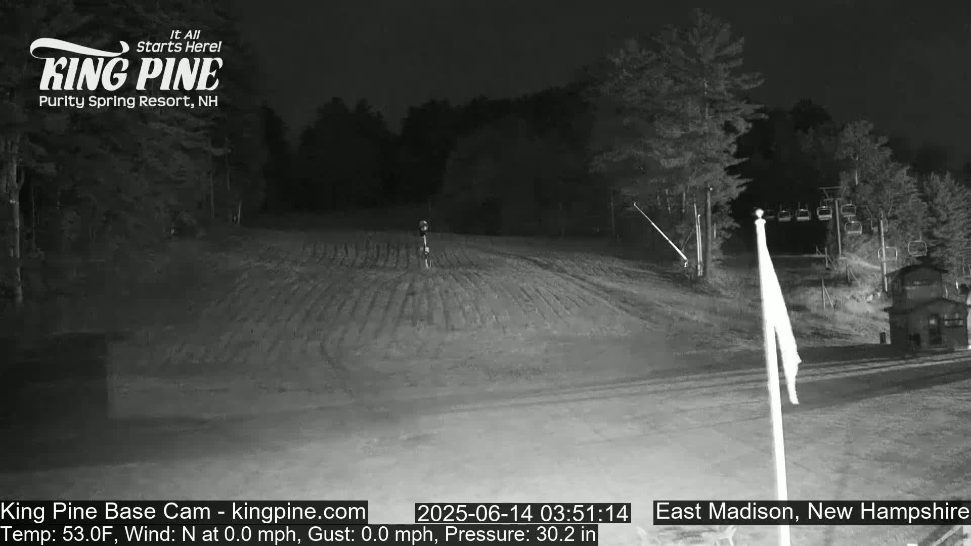 A nighttime view of a mostly empty ski slope with trees in the background under clear skies.