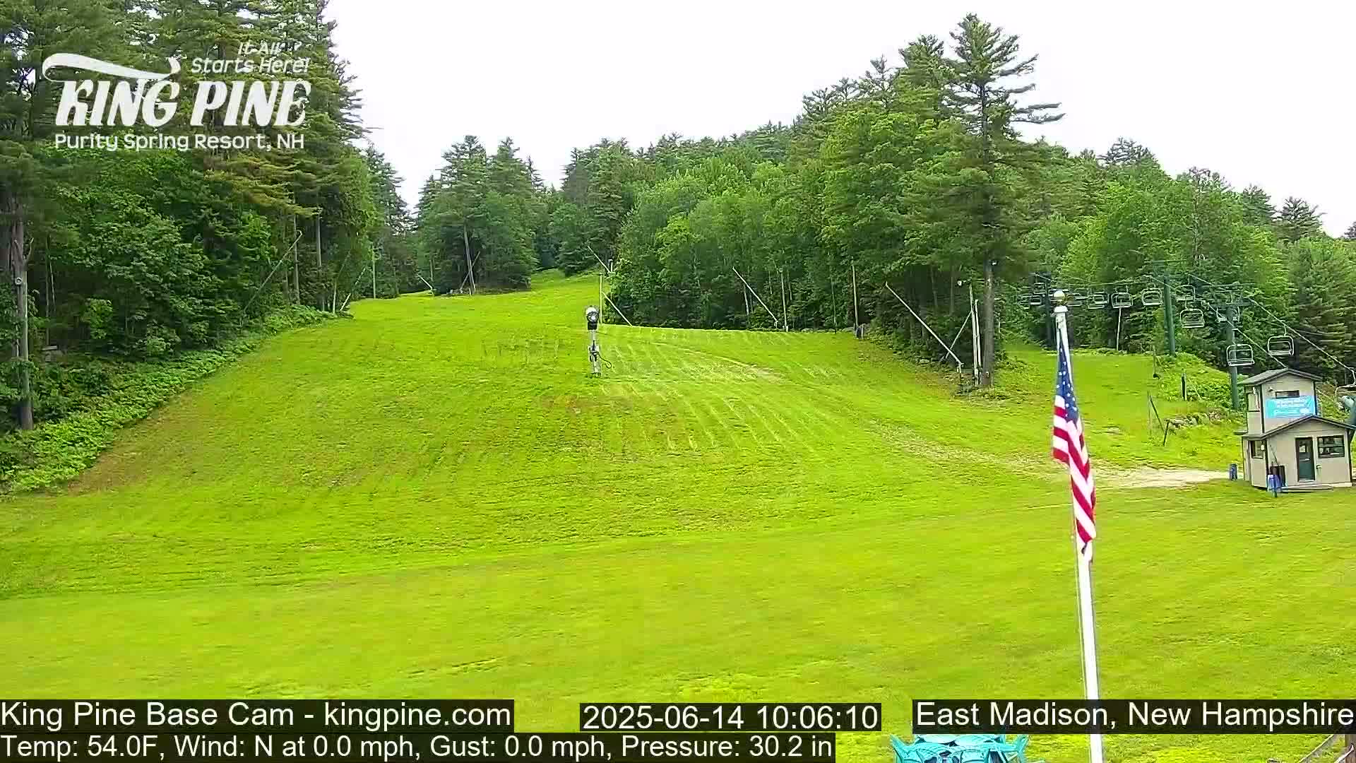 A grassy hill with a ski lift and a few people visible in the distance, under a partly cloudy sky.