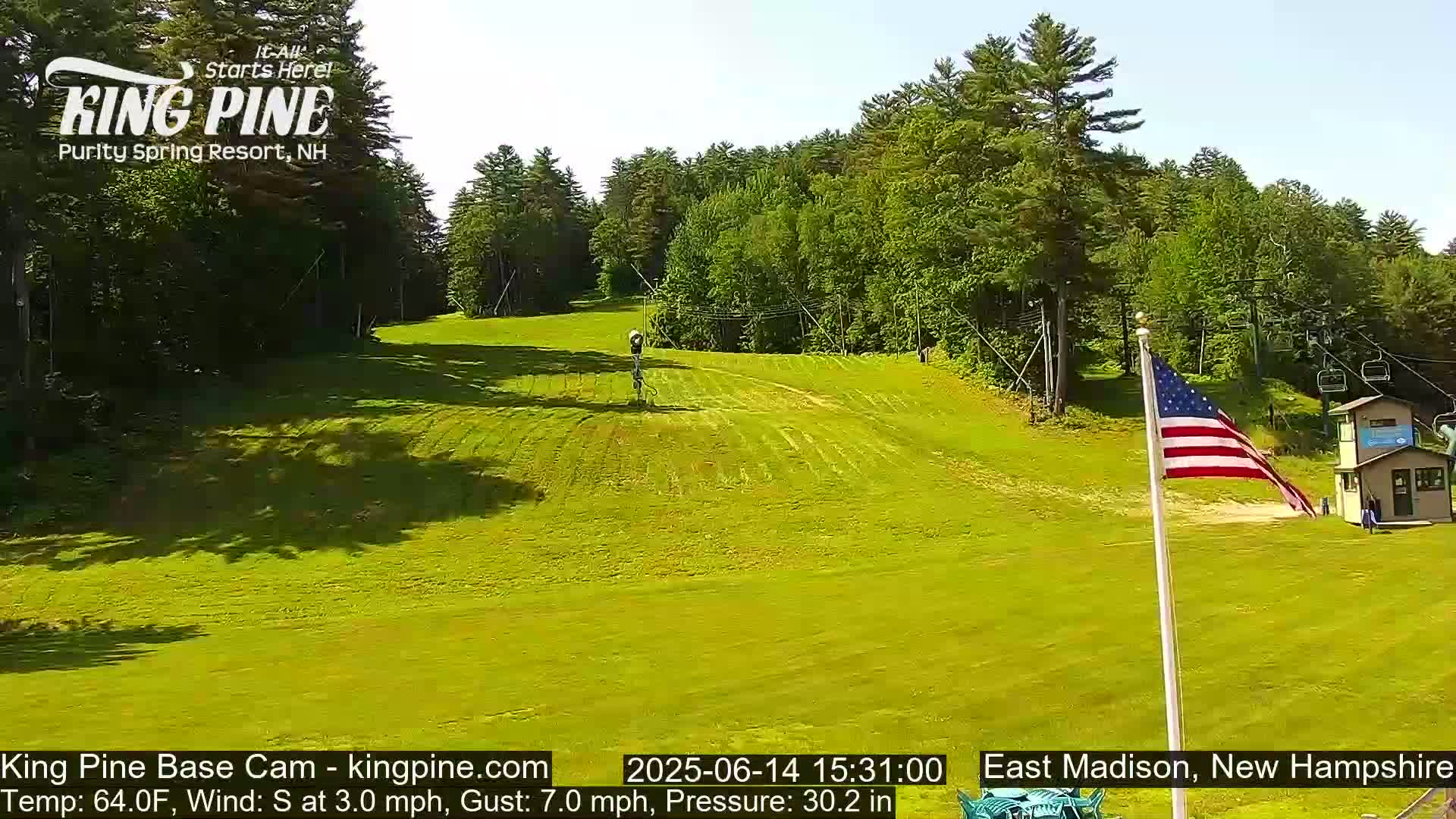 A grassy hill with a ski lift and a few people visible in the distance, under a partly cloudy sky.