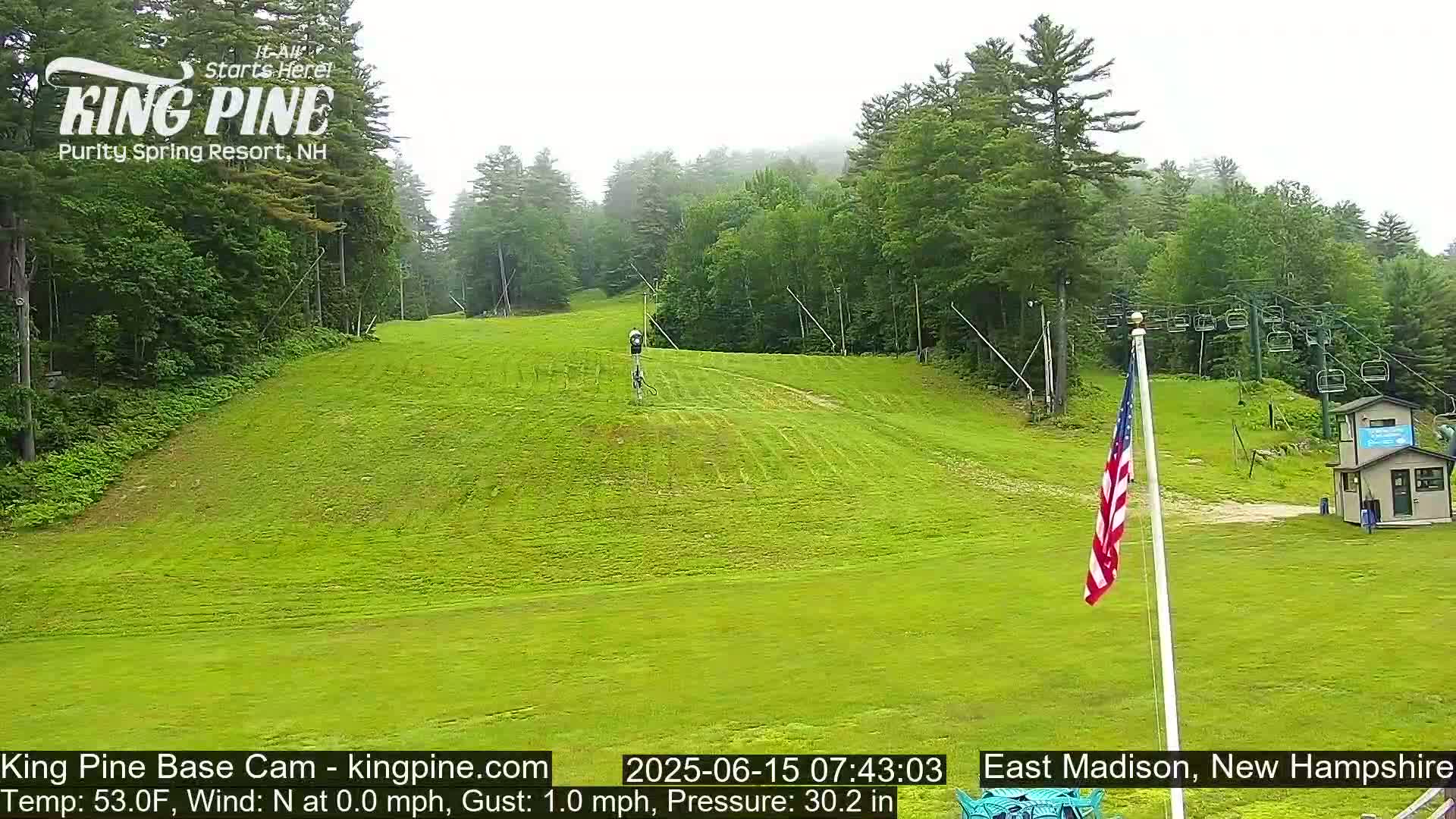 A grassy ski slope, mostly empty, is visible under an overcast sky, with a chairlift and a small building in the background.