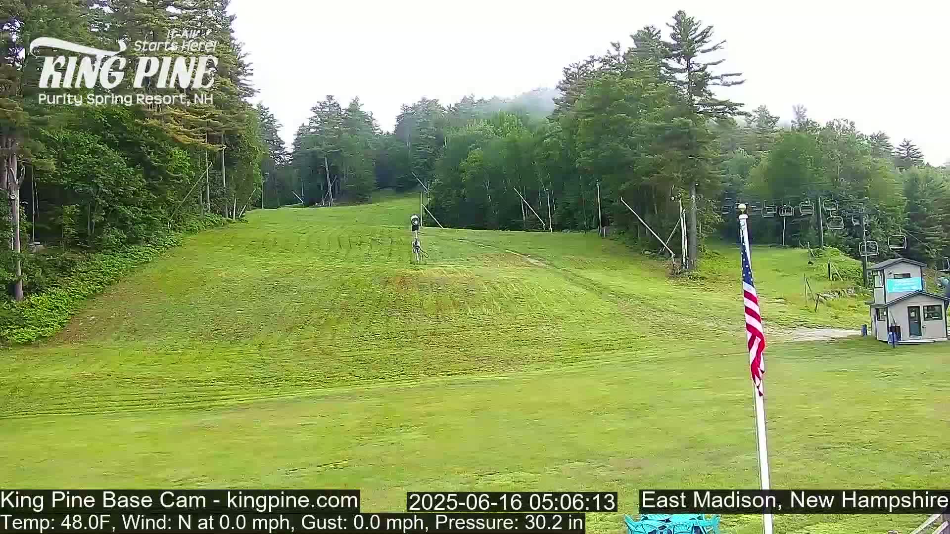 A grassy ski slope with a chairlift and an American flag, on an overcast day.