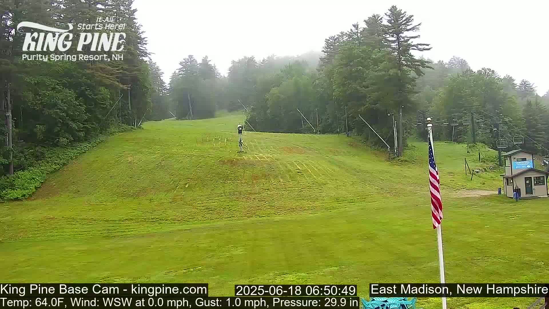 A grassy ski slope with a chairlift and an American flag is visible on an overcast day.