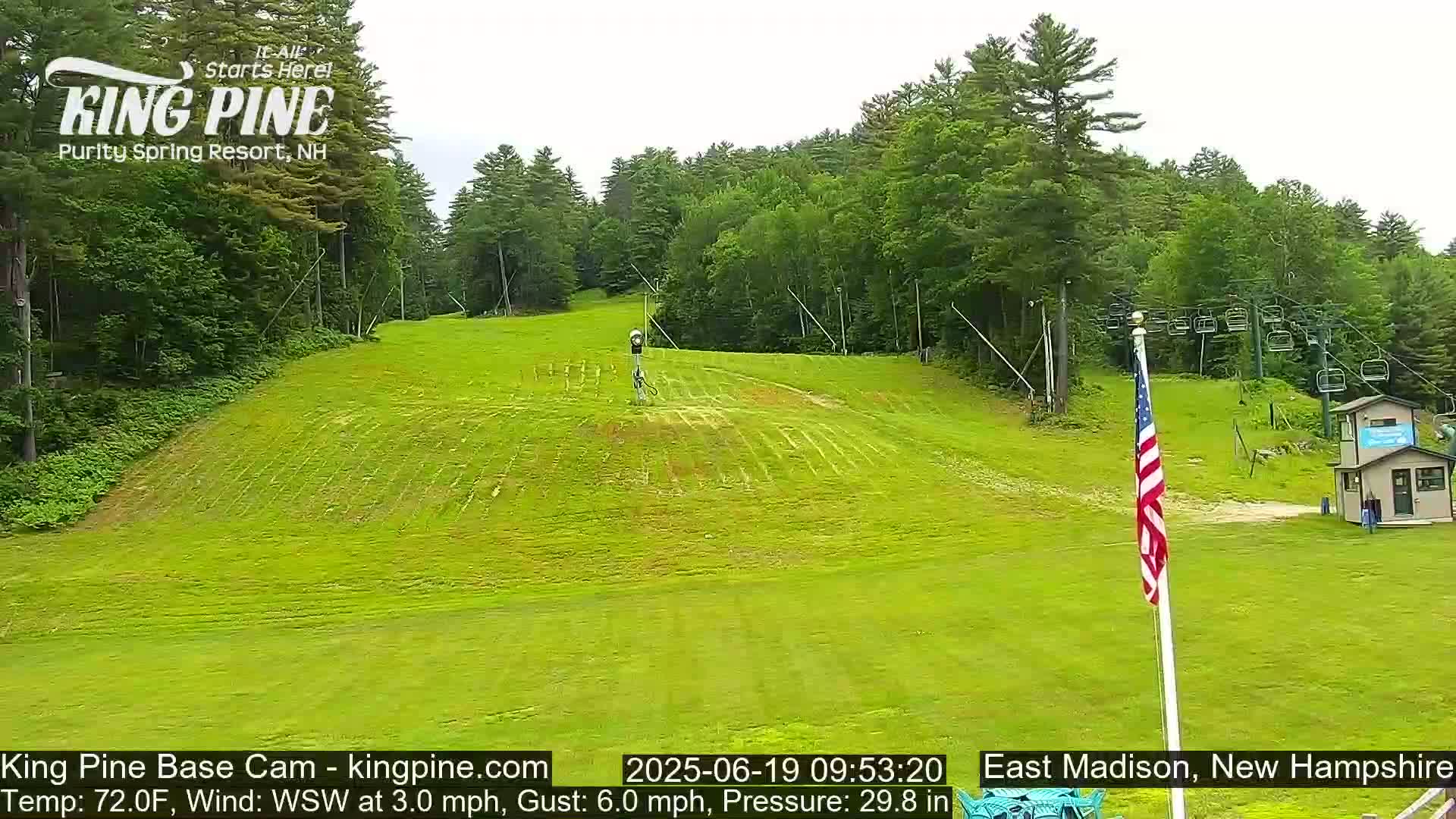 A grassy ski slope is visible, with a chairlift and a small building in the background, under partly cloudy skies.