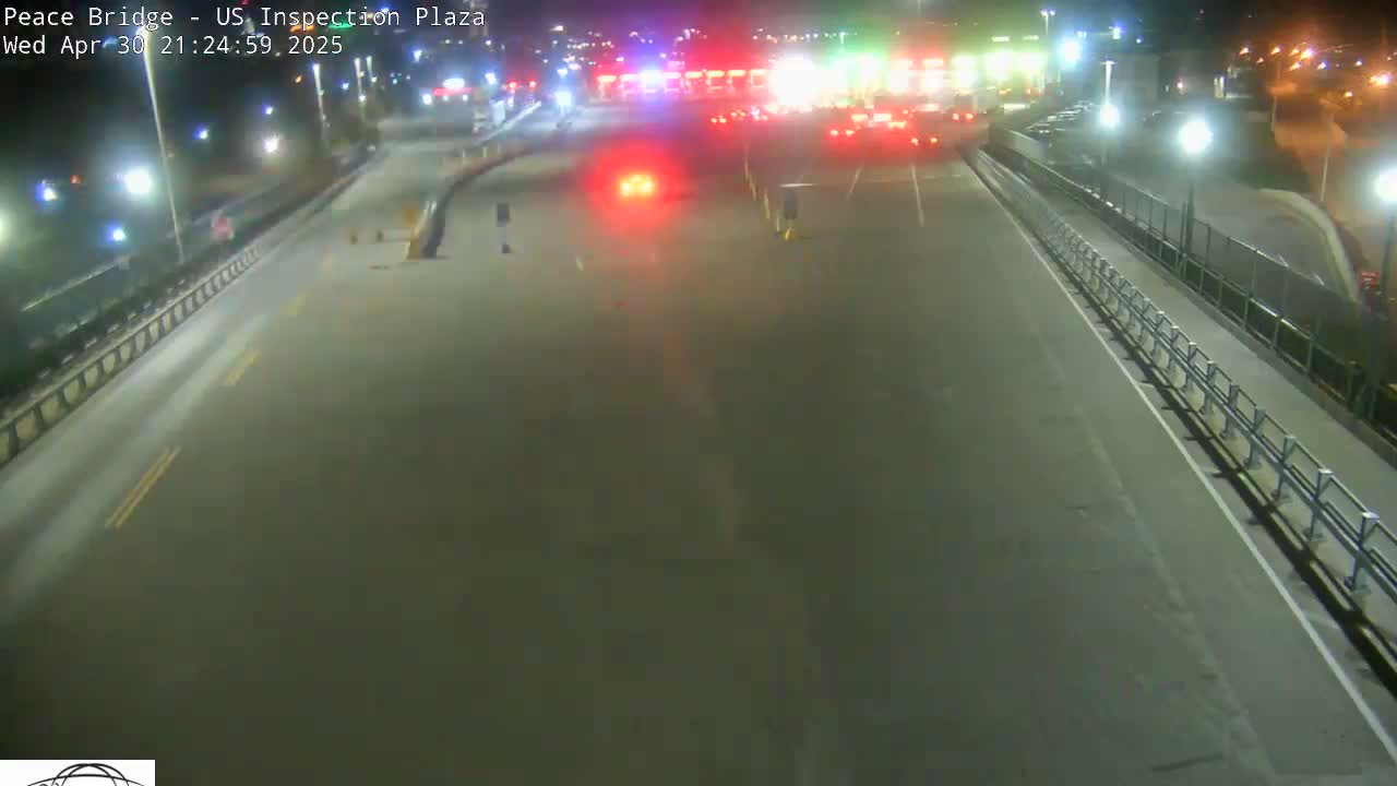 A nighttime, overhead view shows a mostly empty roadway leading to a border crossing inspection plaza with a few vehicles visible.