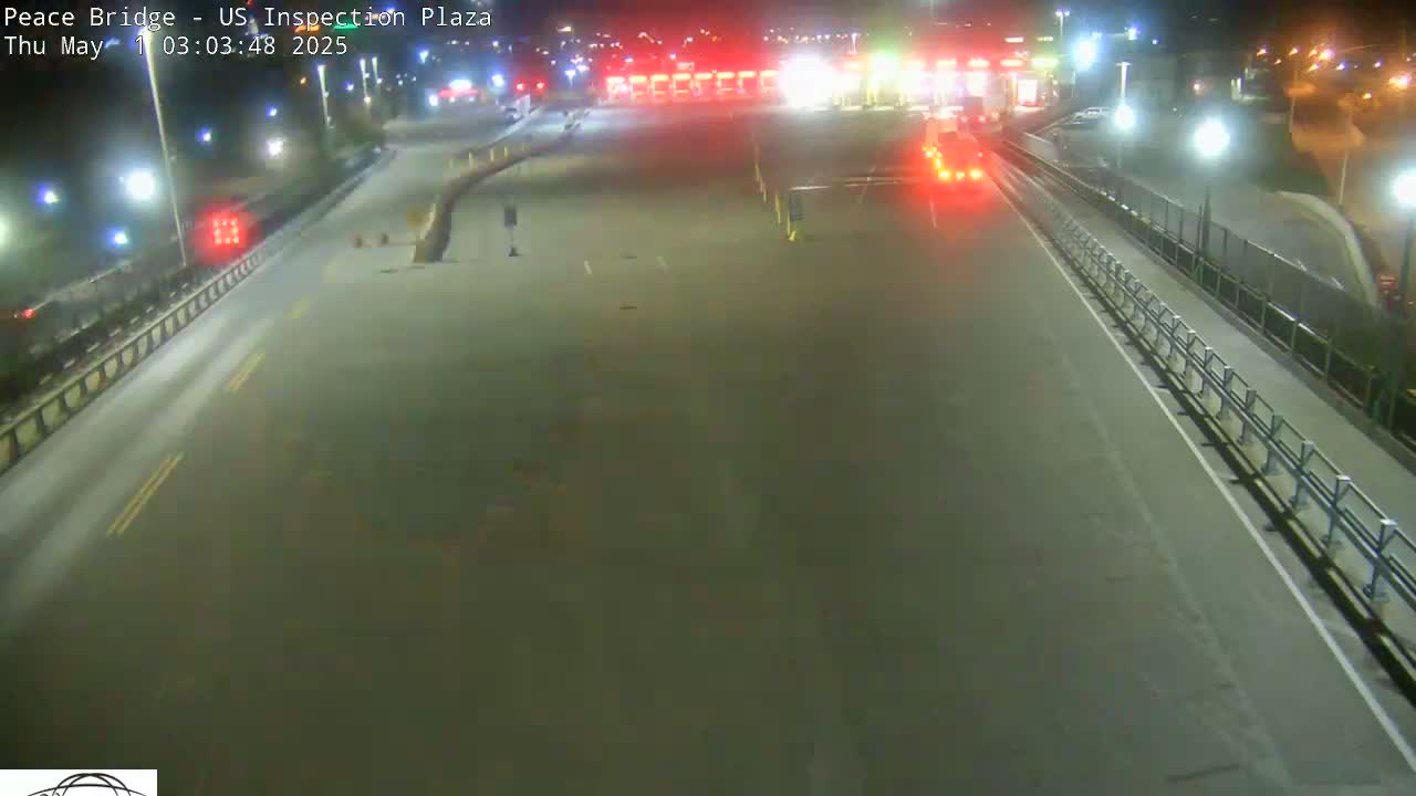 A nighttime, high-angle view shows a mostly empty highway leading to a border inspection plaza with a few vehicles visible.