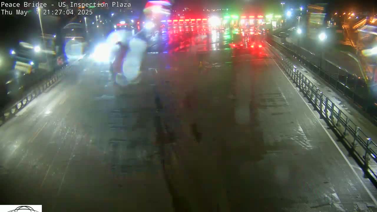 A wet, nighttime scene shows a roadway with vehicles and a barrier, under dim lighting.