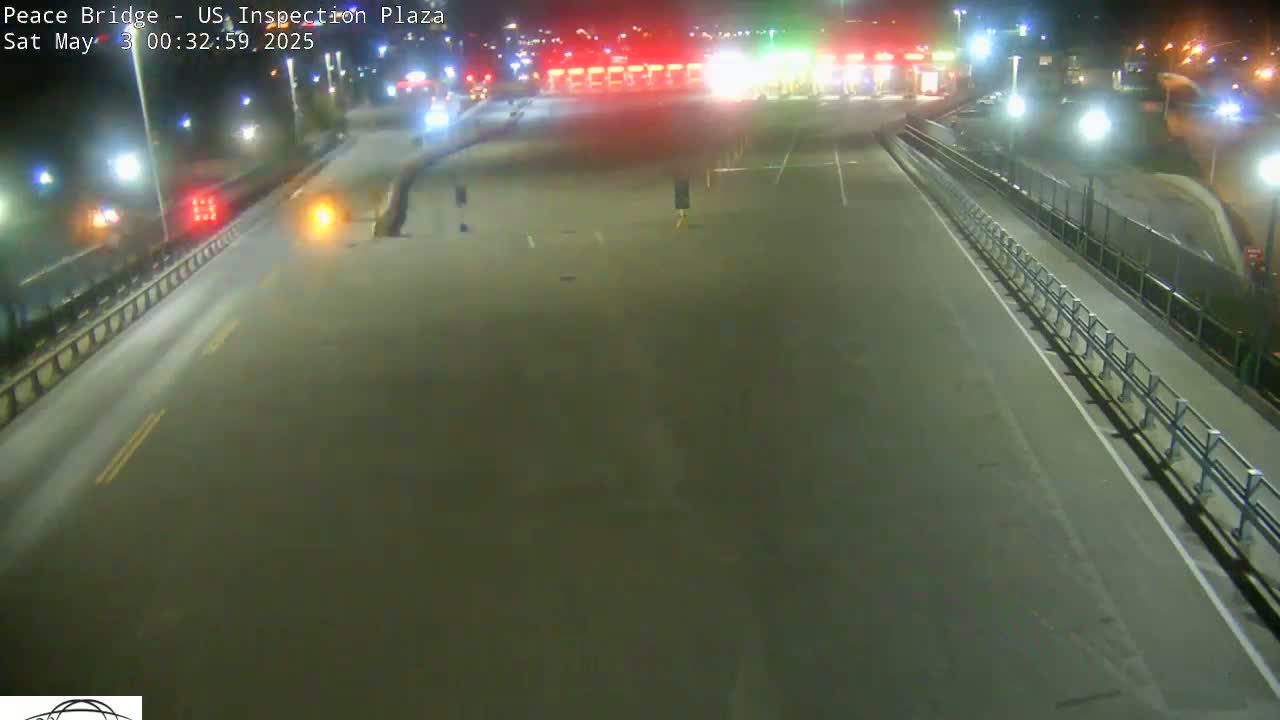 A nighttime view of an empty roadway leading to a border inspection plaza under artificial lighting.