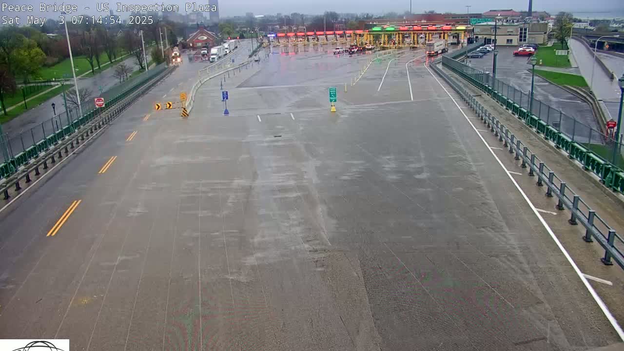 A wet, empty roadway leads to a border crossing inspection plaza on an overcast day.