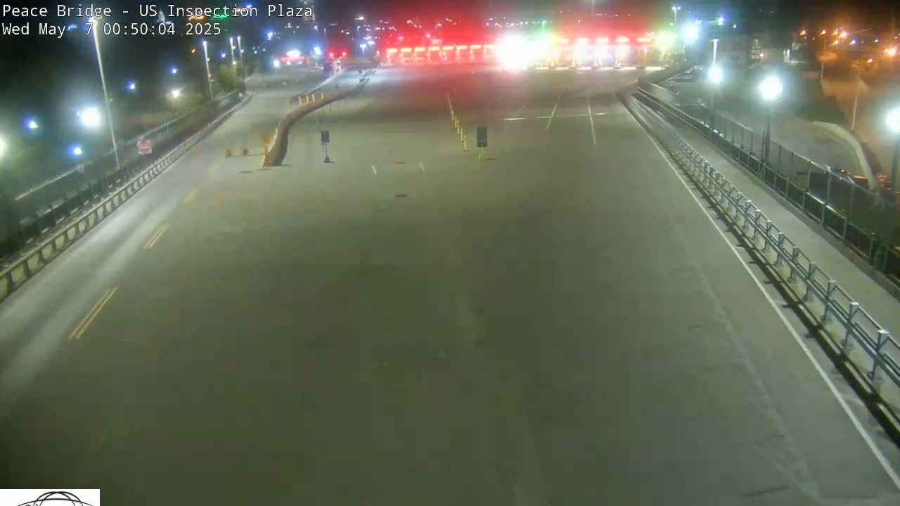 An empty roadway at night leads to a brightly lit border crossing checkpoint under dark, clear skies.