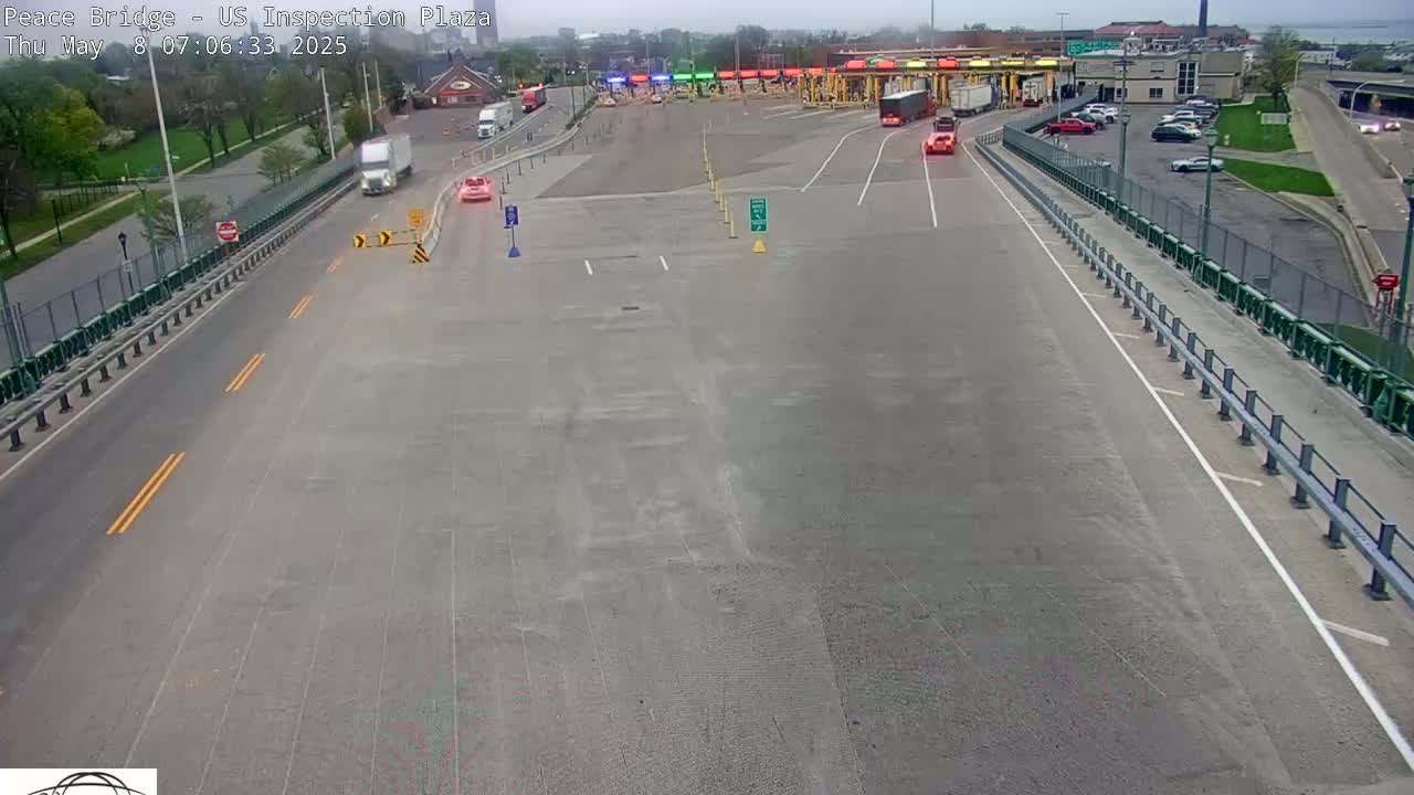 A mostly empty highway approaches a border crossing inspection plaza on an overcast day, with a few vehicles visible.