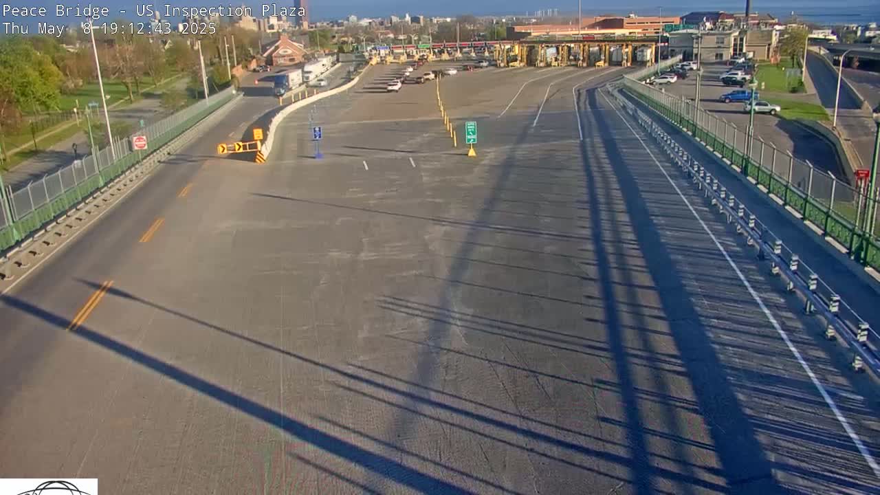 An empty highway leads to a mostly empty parking lot at a border inspection plaza on a sunny day.