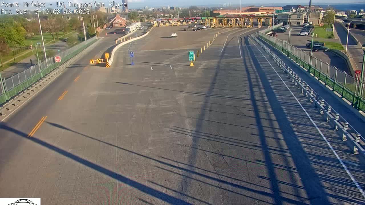 A mostly empty highway approaches a border inspection plaza on a sunny day, with long shadows cast across the road.