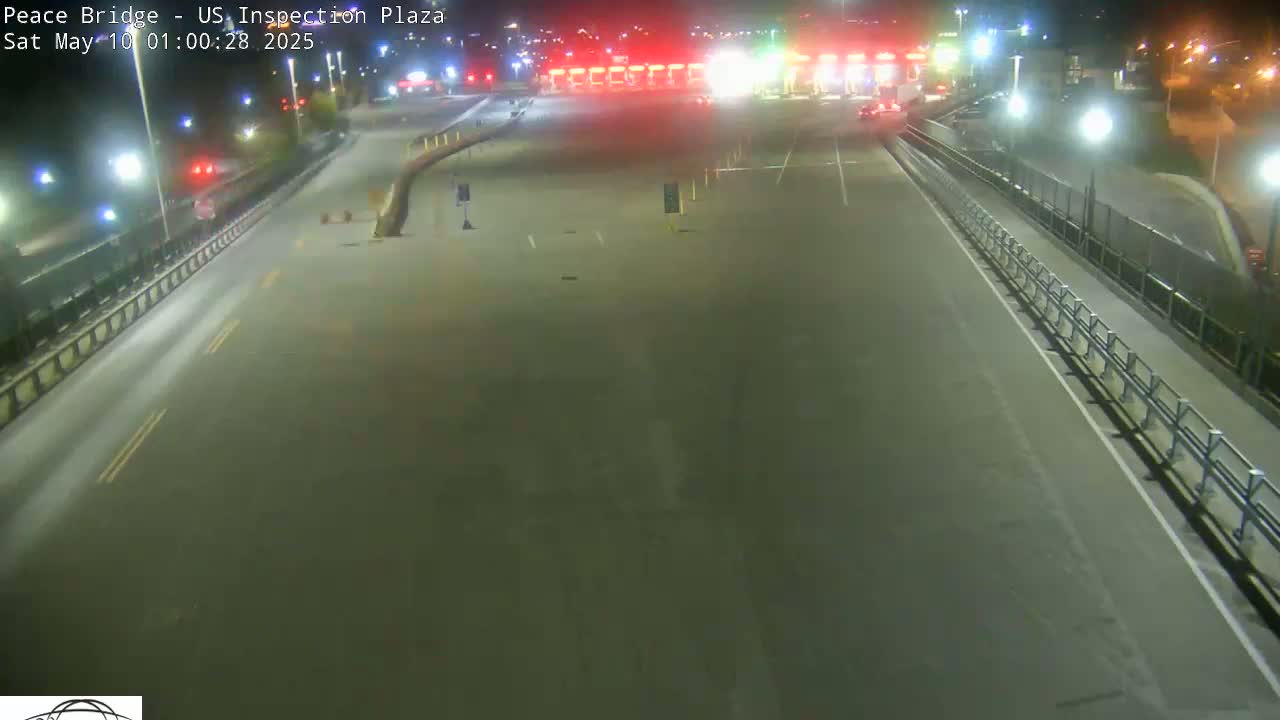 A mostly empty roadway at night leads to a brightly lit border inspection plaza.