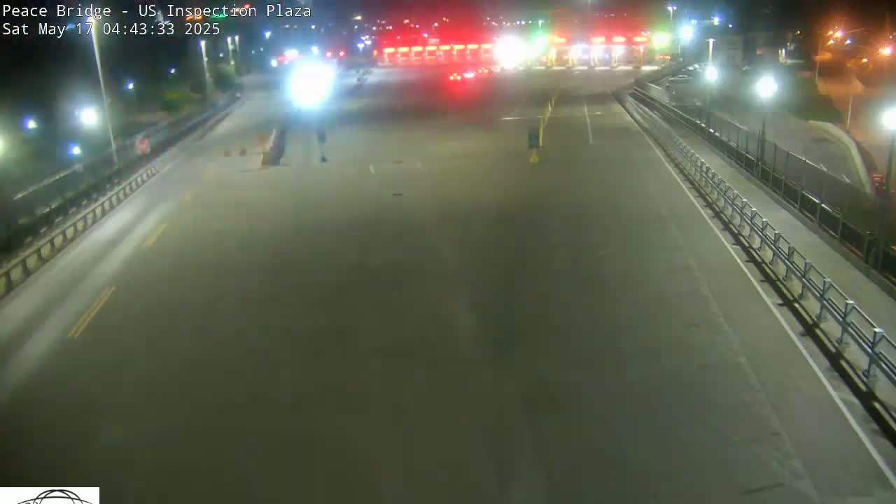 A nighttime view of an empty highway leading to a border inspection plaza with a few vehicles visible in the distance under artificial light.