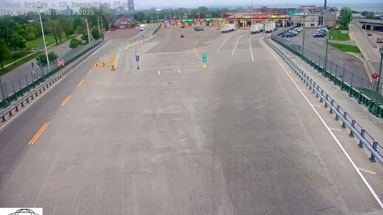 An empty roadway approaches a border inspection plaza on a partly sunny day.