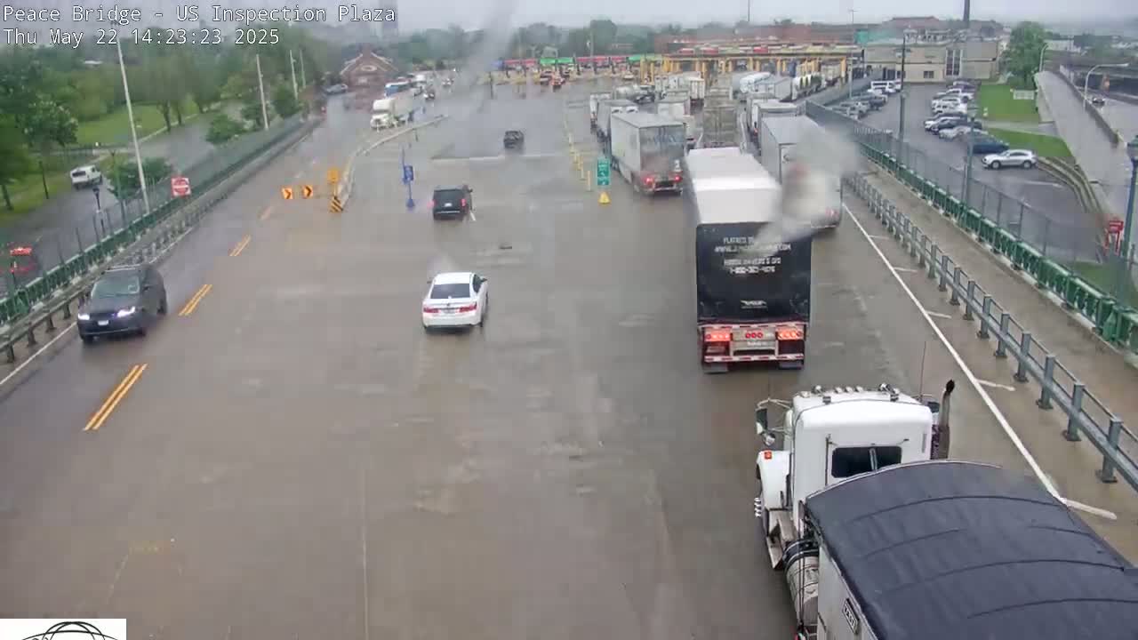 A rain-soaked roadway shows several cars and semi-trucks navigating a border inspection plaza.
