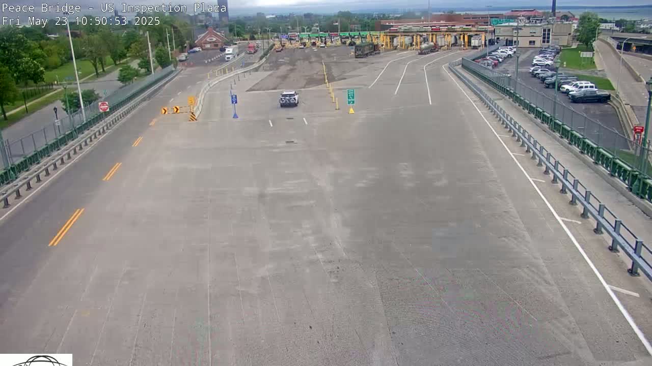 A mostly empty highway approaches a border crossing inspection plaza on a partly cloudy day.