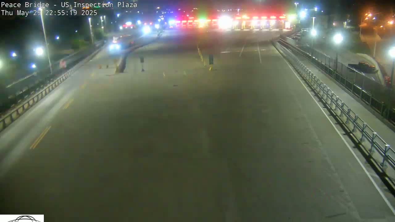 A nighttime view of an empty roadway leading to a brightly lit border inspection plaza.