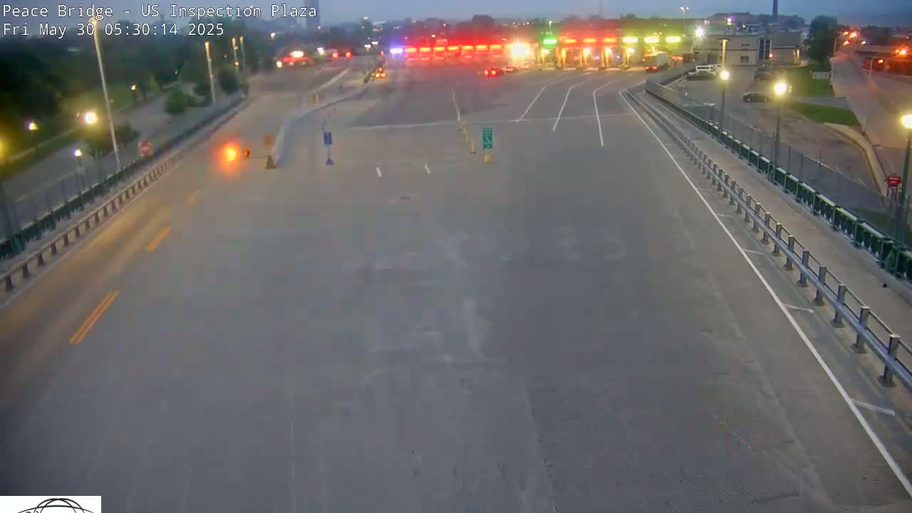 A mostly empty roadway leading to a border inspection plaza at twilight, with a few vehicles visible.