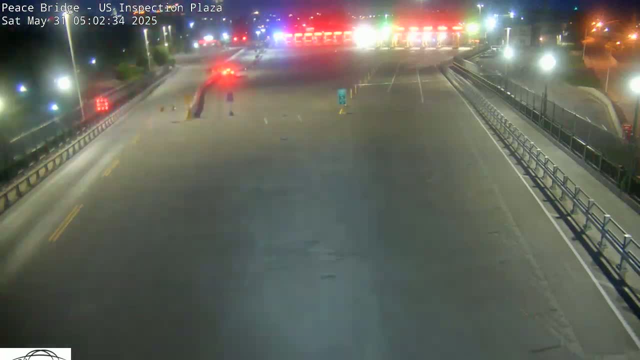 A nighttime view of an empty highway leading to a border inspection plaza with minimal traffic.