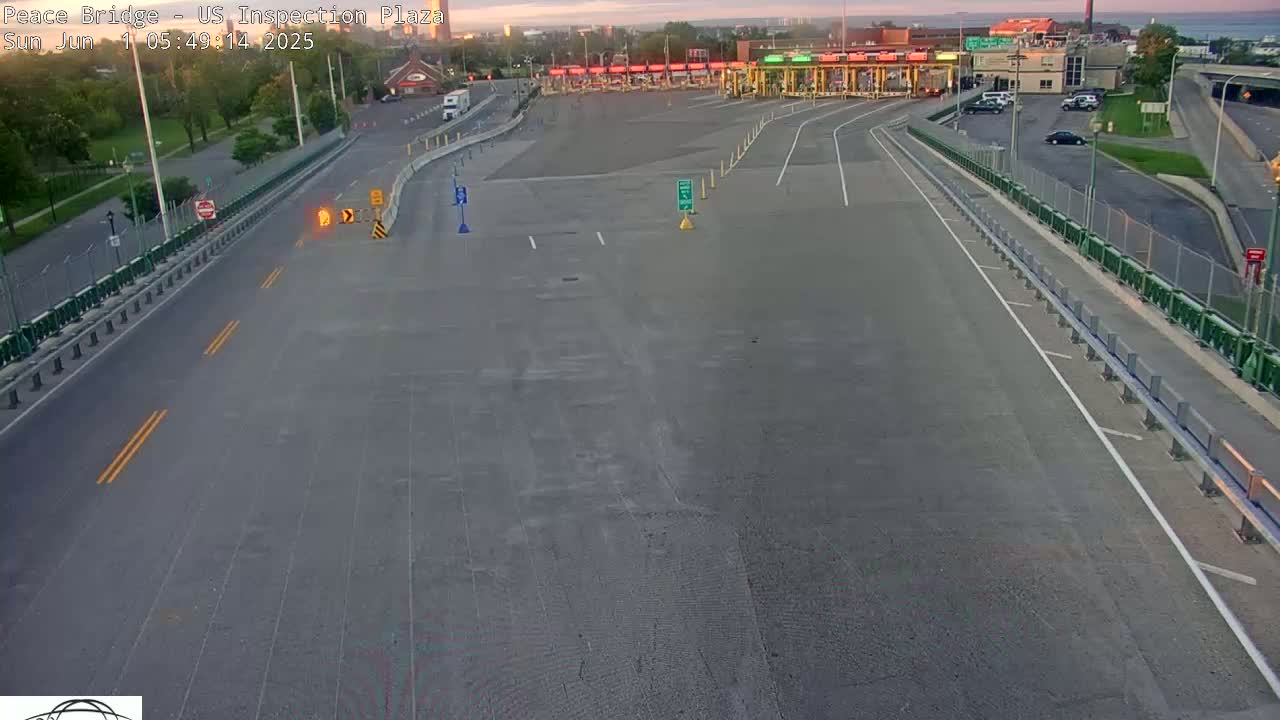 An empty roadway leads to a border inspection plaza under a clear sunrise sky.