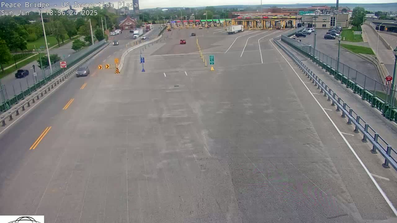 A mostly empty highway approaches a border crossing inspection plaza on a partly cloudy day.