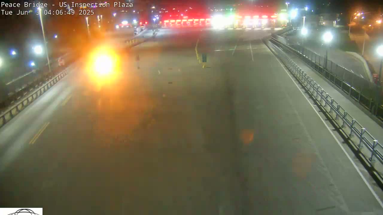 A nighttime, hazy view of an empty roadway leading to a brightly lit inspection plaza.