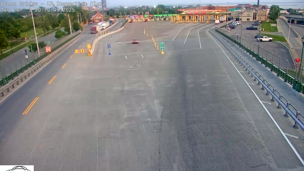 A mostly empty US inspection plaza at the Peace Bridge on a sunny day, with a few vehicles visible on the roads and in parking lots.