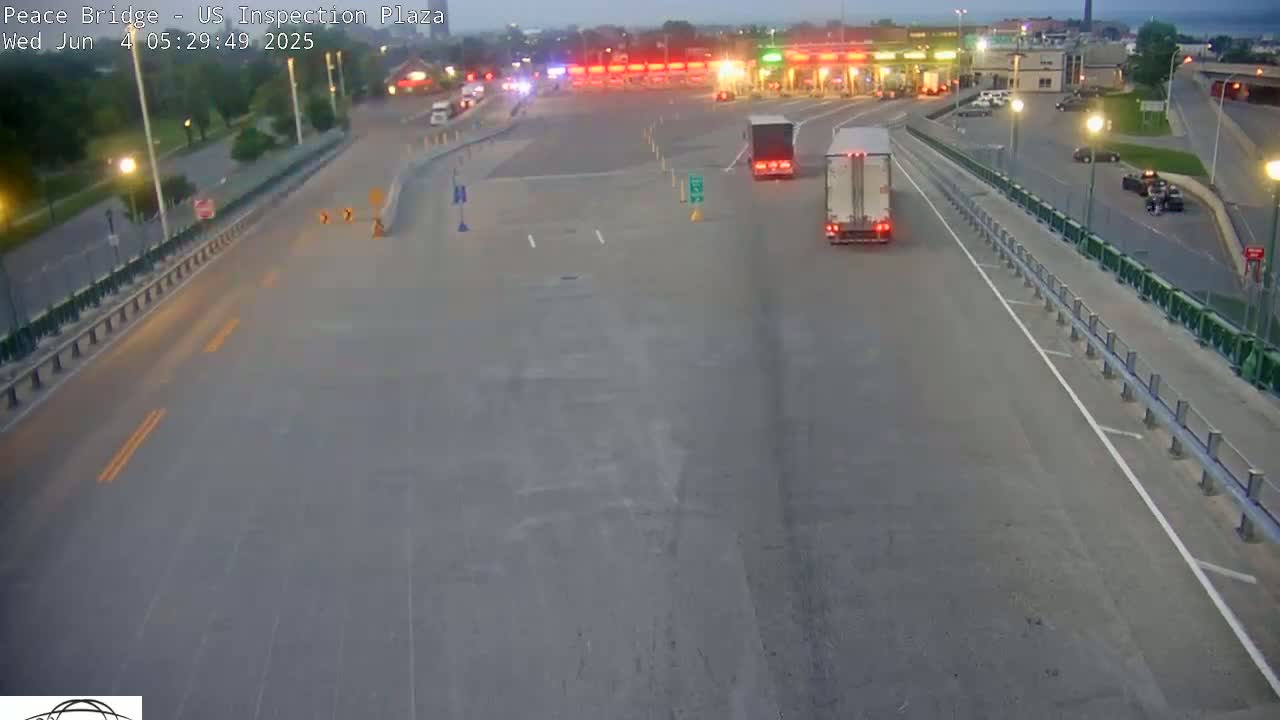 Several vehicles are traveling on a highway approaching a toll plaza under a twilight sky.