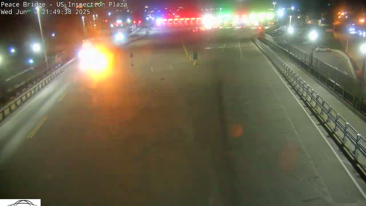 A brightly lit nighttime scene shows a roadway leading to a toll plaza, with a vehicle emitting a bright orange glow in the foreground.