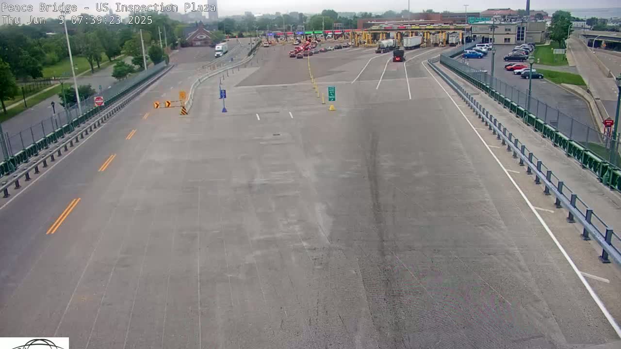 A mostly empty roadway leads to a border inspection plaza on a partly cloudy day.