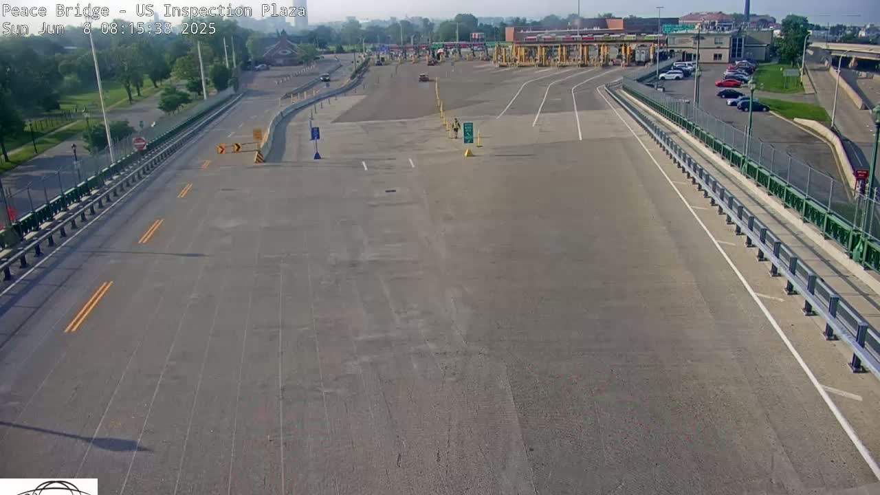 A mostly empty US inspection plaza on a sunny day, with a few cars visible in the parking lot and approaching the toll booths.