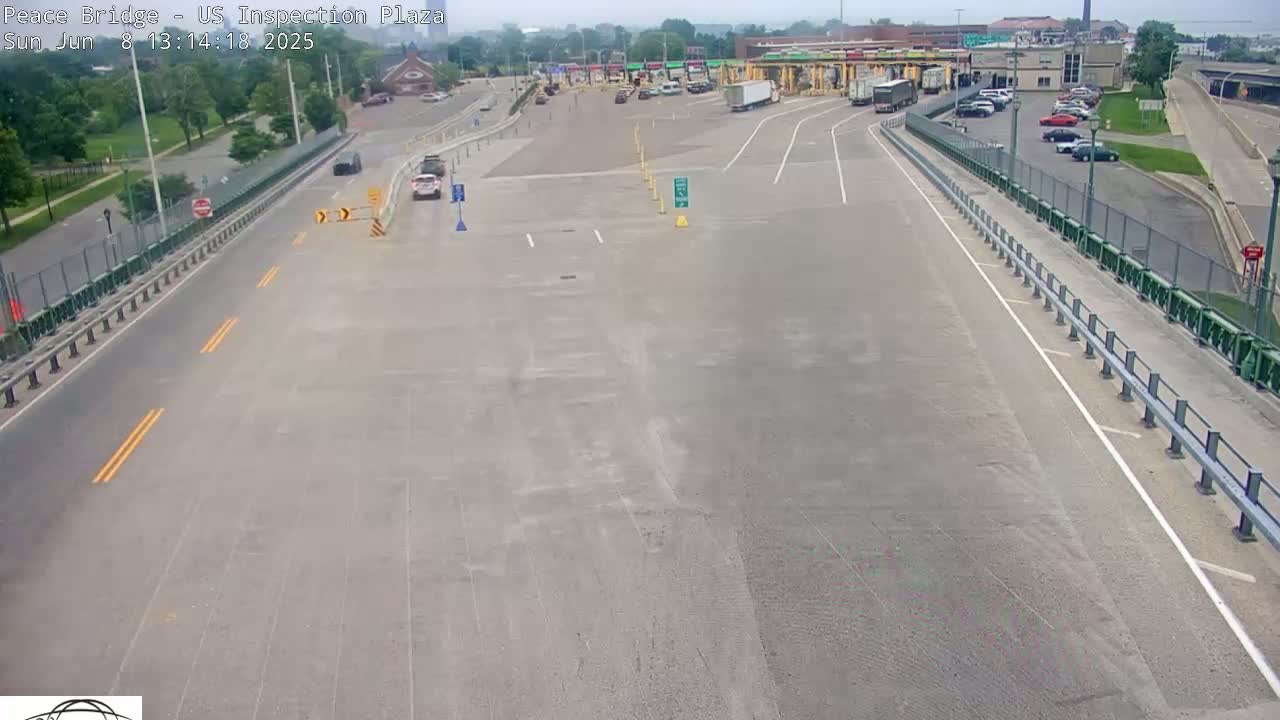 A mostly empty US inspection plaza is viewed from above on a sunny day, with a few cars visible on the roads leading to and from the plaza.