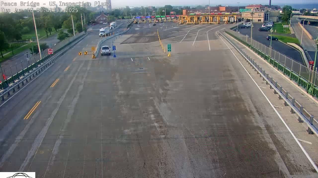A mostly empty US border inspection plaza on a sunny day, with a few cars visible on the roads leading to and from the plaza.