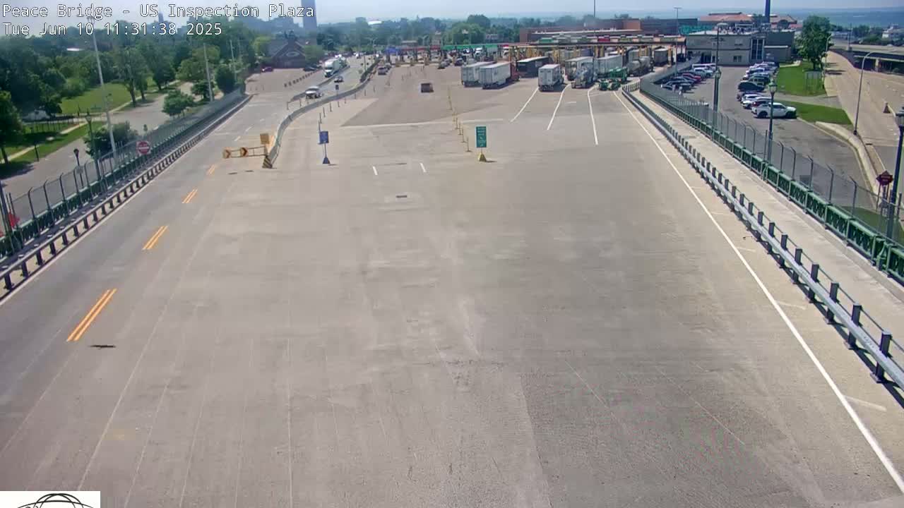 An empty roadway leading to a border inspection plaza with several parked vehicles and trucks under a clear sky.