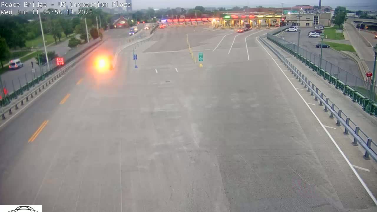 A high-angle, long shot of a mostly empty highway leading to a border inspection plaza on an overcast day.