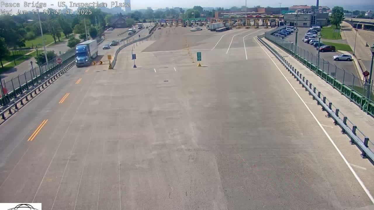 An overhead view shows a mostly empty US inspection plaza on a sunny day with a semi-truck and several cars visible.