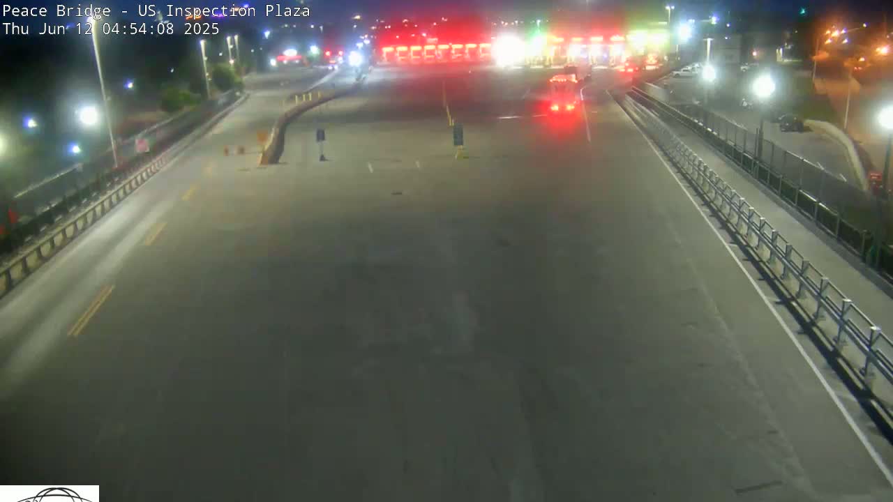 A nighttime, overhead view of a mostly empty highway leading to a brightly lit toll plaza.