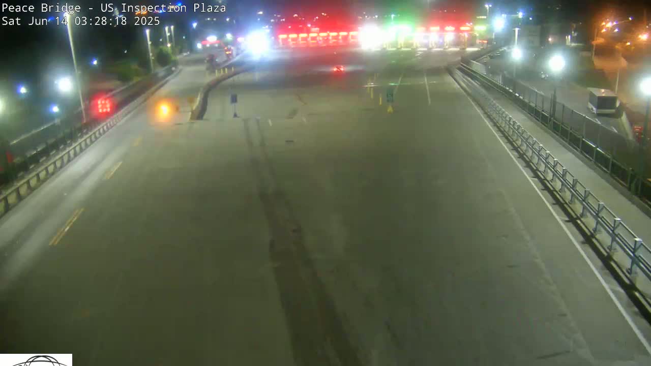 A mostly empty, brightly lit highway at night leads to a border inspection plaza.