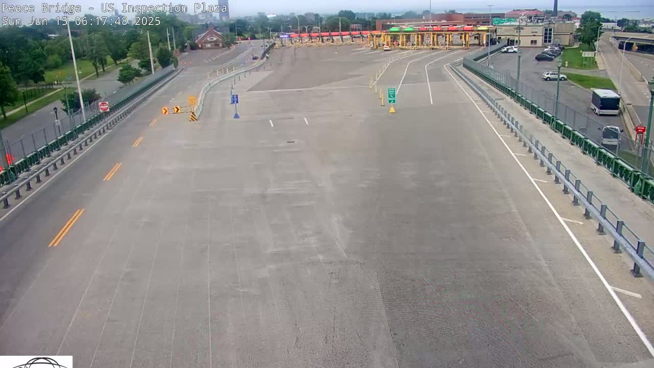 An empty highway approaches a border inspection plaza on a sunny day, with a few vehicles visible in the parking lot.