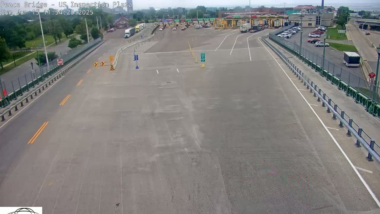 A mostly empty US customs inspection plaza on a sunny day with several vehicles in the parking lot and a few on the road.