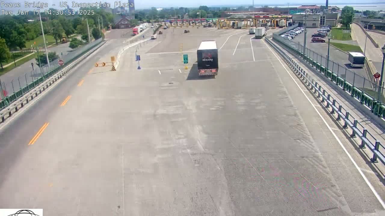 A mostly empty US inspection plaza on a sunny day, with a semi-truck in the center and several cars parked nearby.