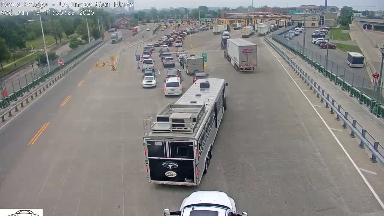 A long line of vehicles waits at a border crossing on a sunny day.