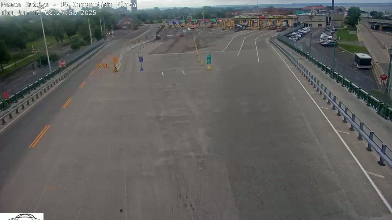 A mostly empty highway approaches a border crossing plaza on a partly sunny day.