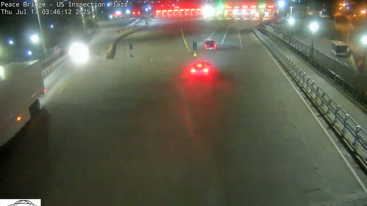 A nighttime, overhead view of a roadway with several vehicles, including a truck and cars, at a border crossing inspection plaza.