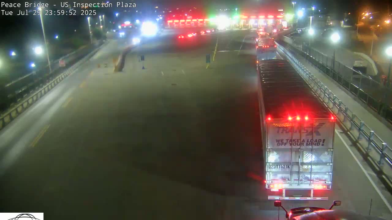 A nighttime, overhead view of a roadway with several vehicles, including a truck and cars, at a border crossing inspection plaza.