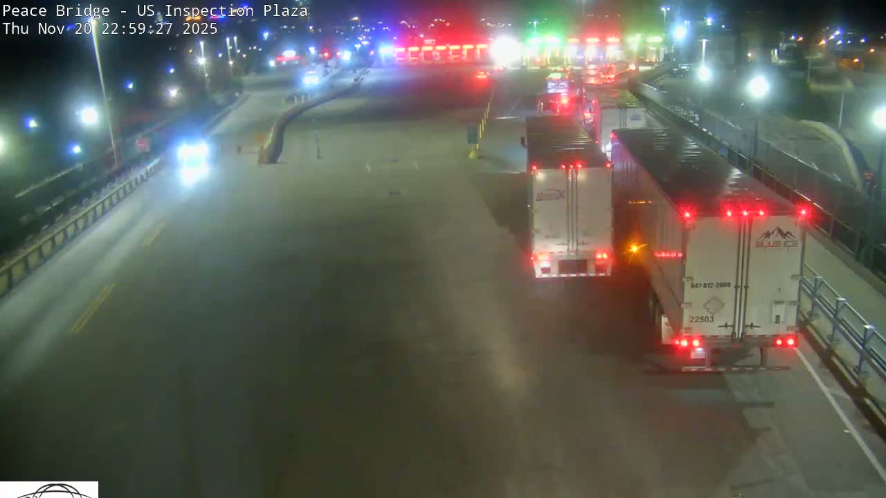 A nighttime, overhead view of a roadway with several vehicles, including a truck and cars, at a border crossing inspection plaza.