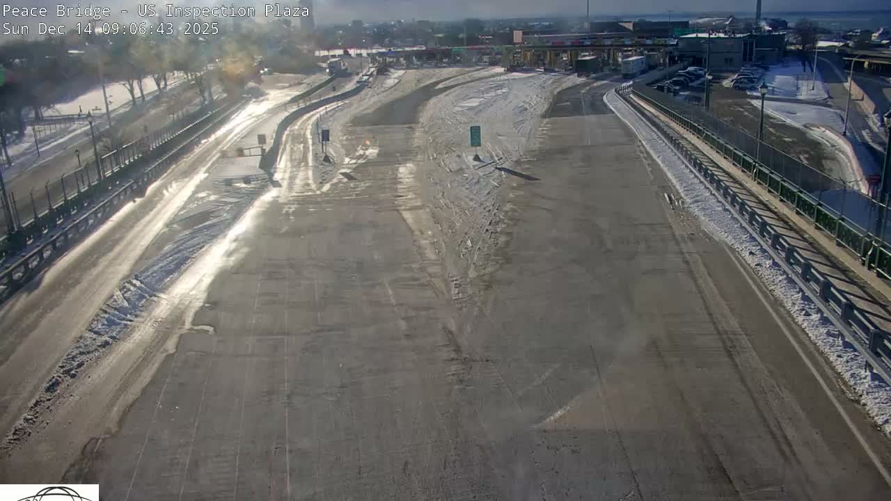 A wet, multi-lane road at night leads to an illuminated inspection plaza with red and green lights, reflecting in the damp pavement.